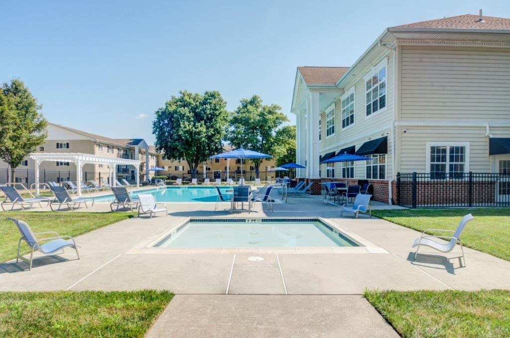 a swimming pool with chairs and umbrellas in front of apartment buildings