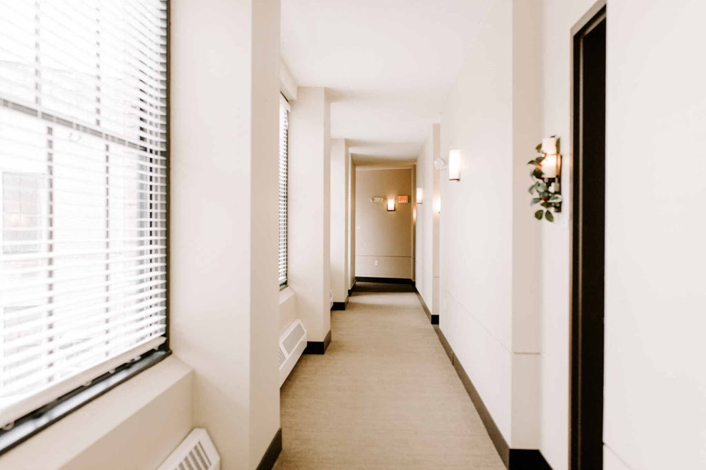 a long hallway with white walls and white blinds and a large window