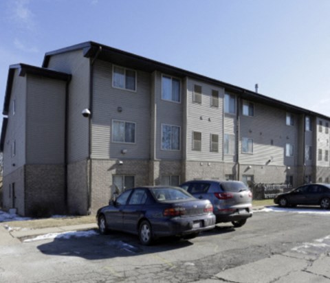A grey apartment building with cars parked in front.