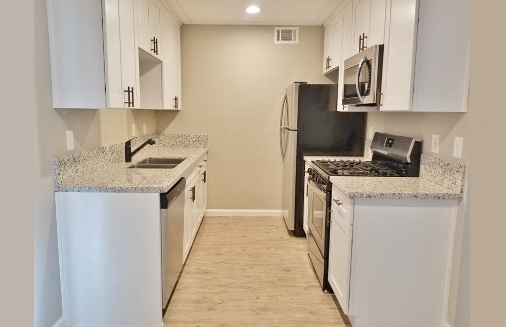 Kitchen view with stainless appliances, white cabinets, stone counters, and wood look flooring.