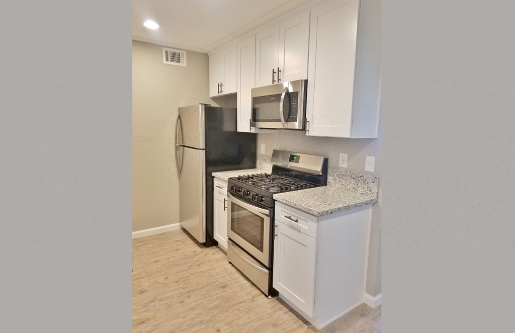 Kitchen view with stainless appliances, white cabinets, stone counters and wood look flooring