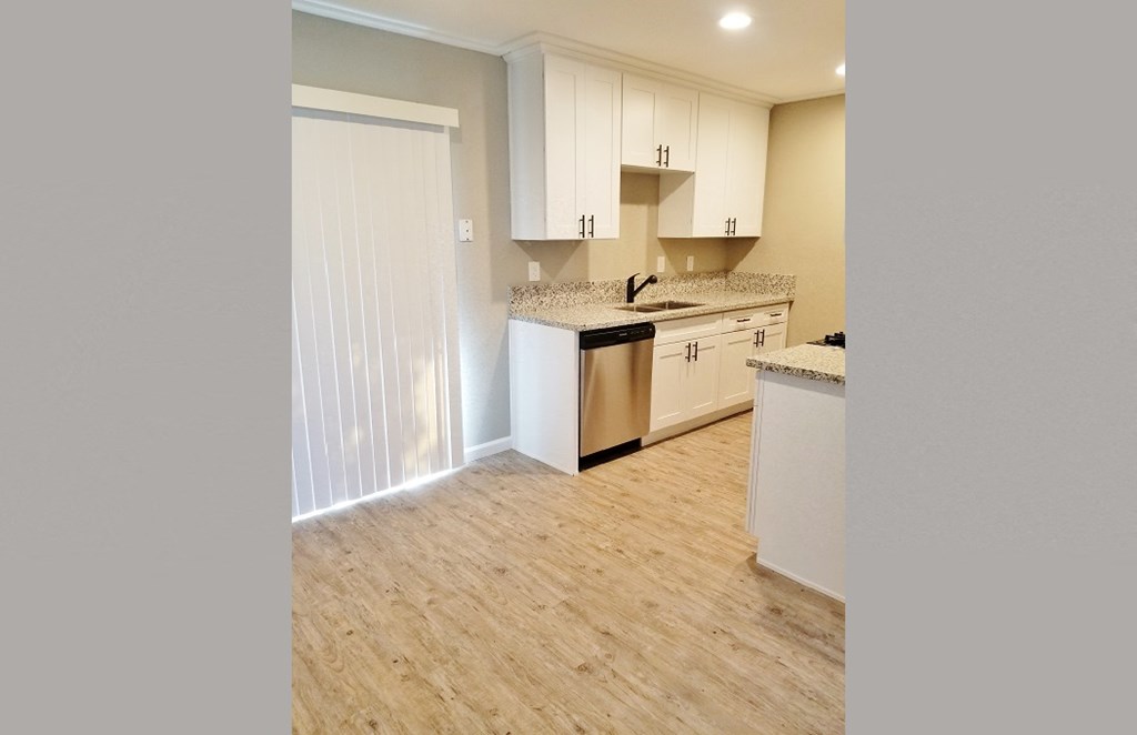 Kitchen view with stainless appliances, white cabinets, stone counters, and wood look flooring.