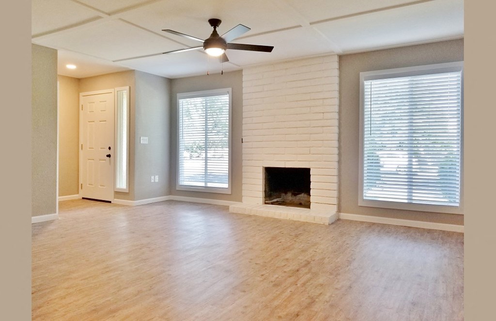 View of living area with wood look flooring, two well lit window, ceiling fan, and wood burning fireplace