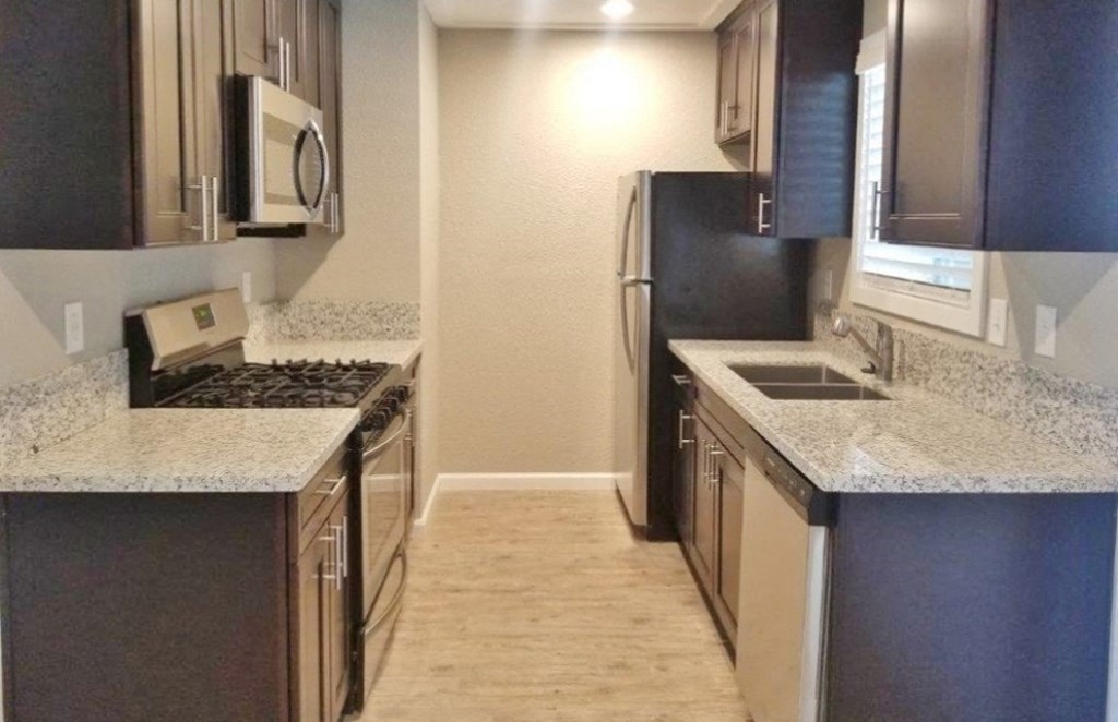Kitchen View View of kitchen with stone counters, stainless appliances, brown cabinets, and wood look flooring