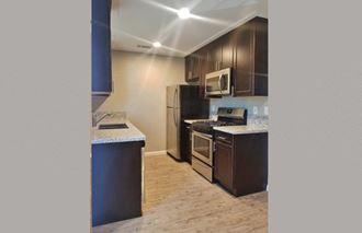 Kitchen area Angled view of kitchen area with brown cabinets, stone counters, stainless appliances and wood look flooring - Photo Gallery