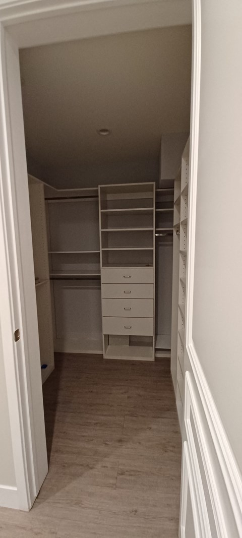 a walk in closet with white shelves and drawers