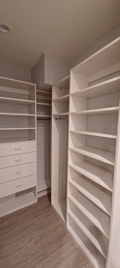 a walk in closet with white shelves and drawers