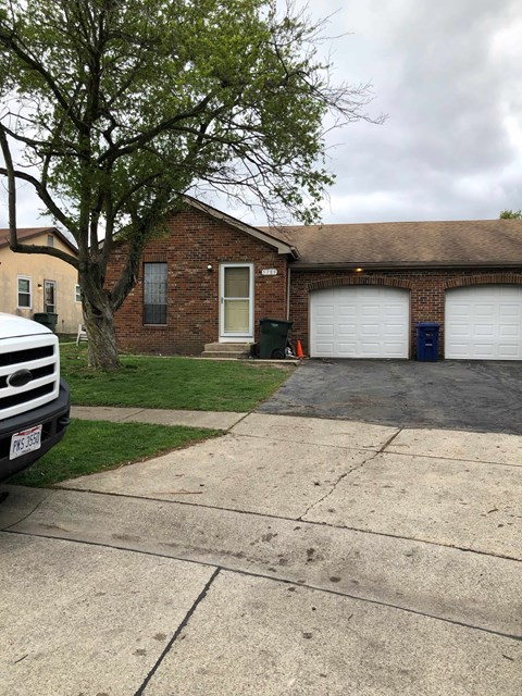 A white car is parked in front of a house with a tree.
