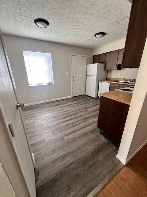 A kitchen with a white fridge and wooden floors.