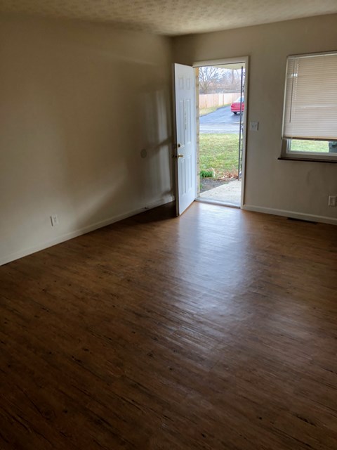 A room with wooden floors and a doorway leading to a driveway.